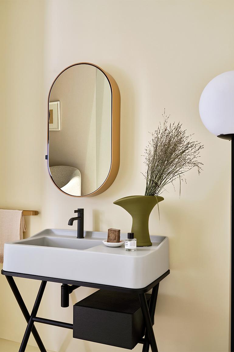 In this image, Siwa by Ceramica CIELO, designed by Andrea Parisio and Giuseppe Pezzano, the cabinet with ceramic washbasin in the Pomice finish of the “Terre di Cielo” colour range combined with a wooden structure with drawer in the Black Oak finish. On the wall the Oval Box mirror with the shell in the Anemone finish.